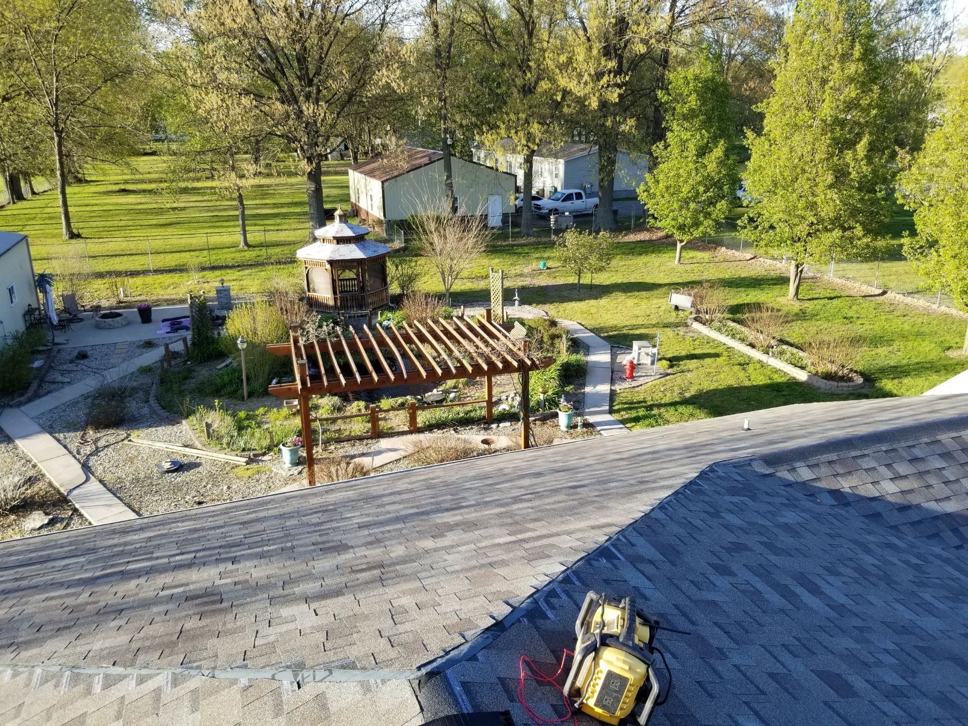 A high-angle view from a roof showing a backyard with a pergola, a gazebo, garden beds, and a nearby house.
