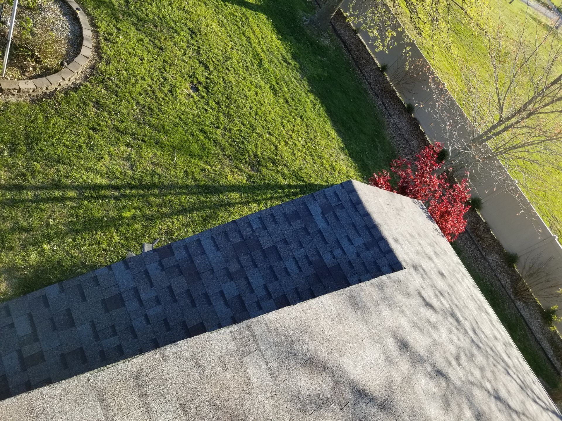 An aerial view of a residential roof with a section of dark shingles and a section of lighter, weathered shingles.