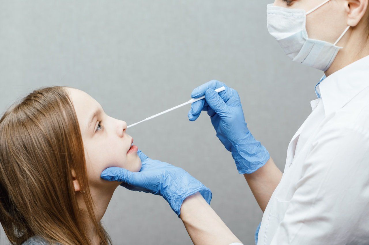 Trabajador médico con mascarilla y guantes realizando un hisopado nasal a un niño en un entorno clínico.