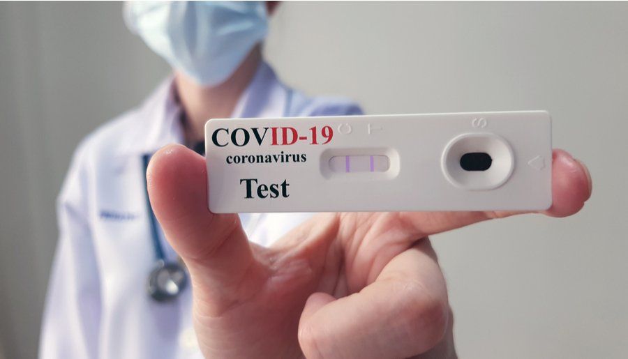 Persona con bata de laboratorio sostiene una prueba de COVID-19 con un resultado positivo.