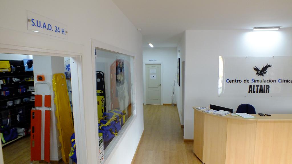 Interior de una clínica médica: mostrador de recepción, pasillo y una sala llena de equipos.