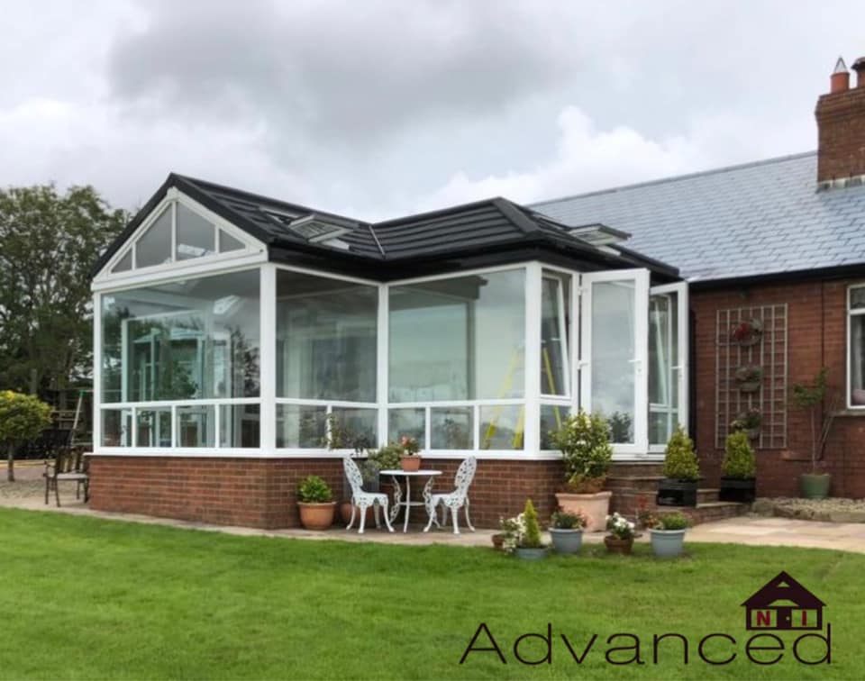 A house with a conservatory and a table and chairs in front of it.