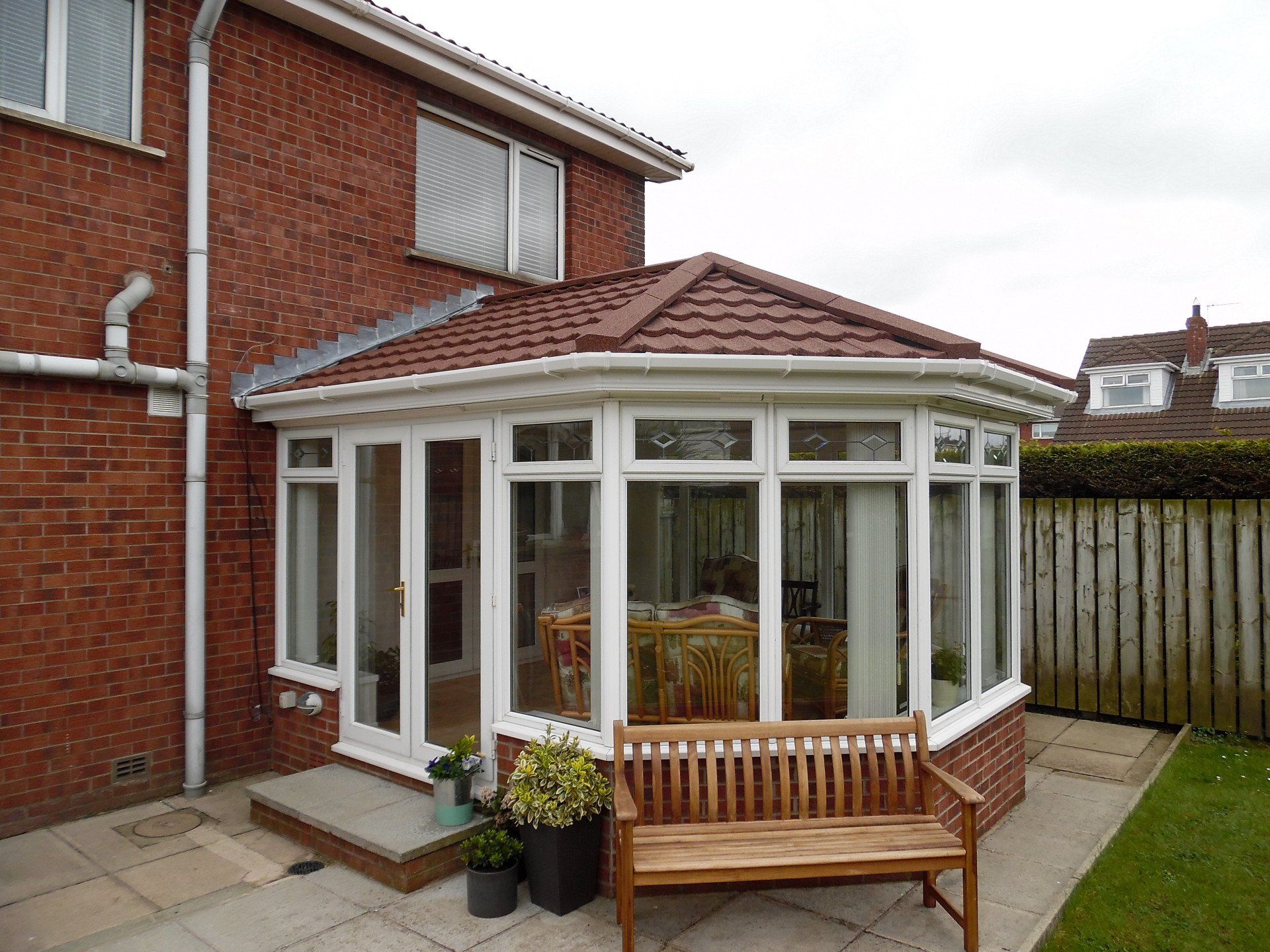 A brick house with a white conservatory and a bench in front of it.