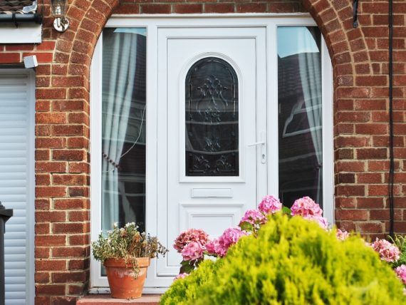 The front door of a brick house with a white door and a potted plant in front of it.