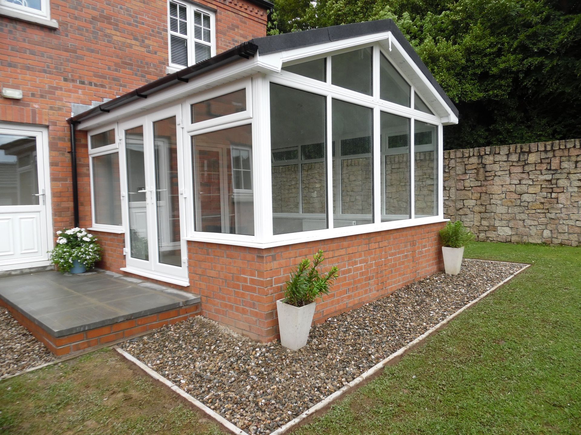 A white conservatory is sitting in the backyard of a brick house.
