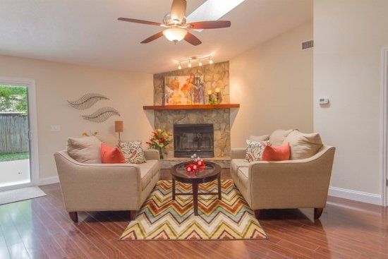 Living room with fireplace, beige sofas, patterned rug, wood floors, and ceiling fan.