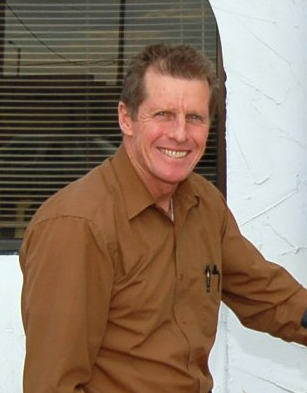 A man in a brown shirt is smiling in front of a window
