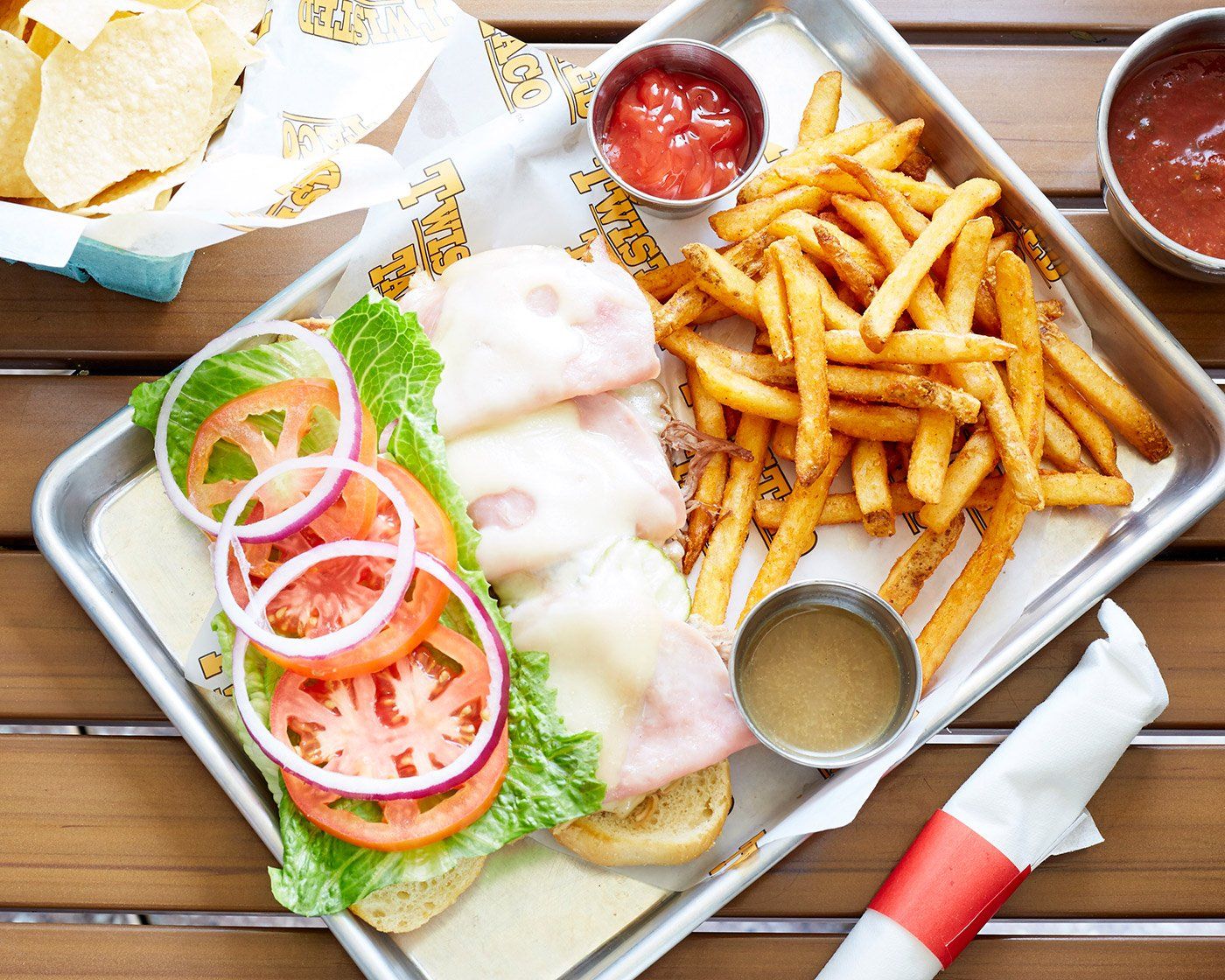 A twisted taco sandwich and french fries on a metal tray on a wooden table.