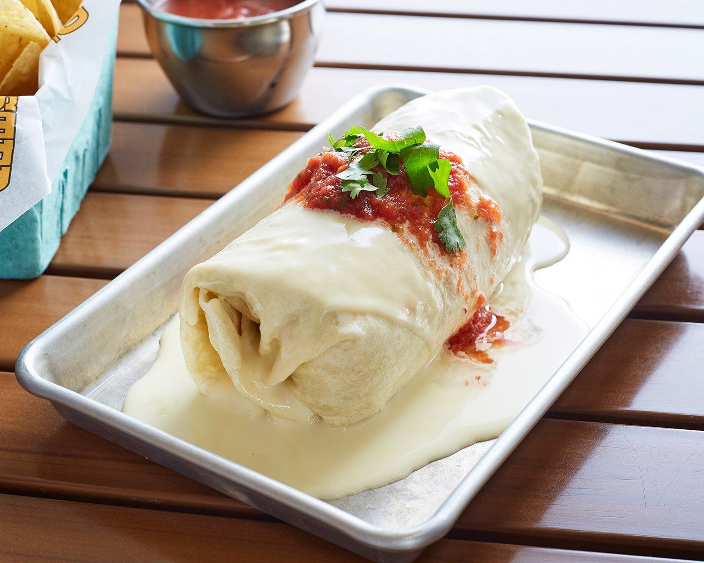 A twisted taco burrito is on a tray on a wooden table