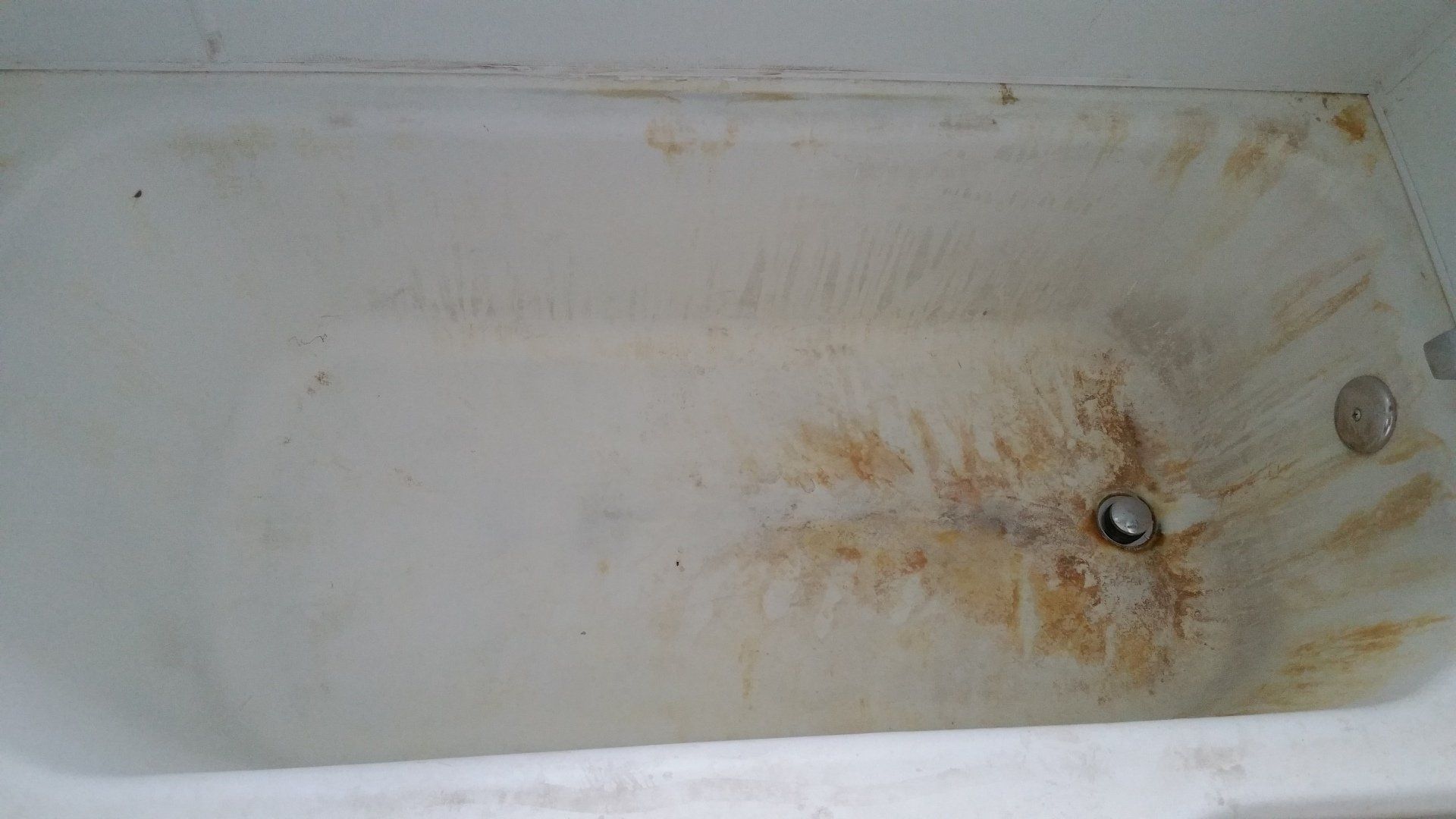 A white bathtub with brown stains on the bottom of it.