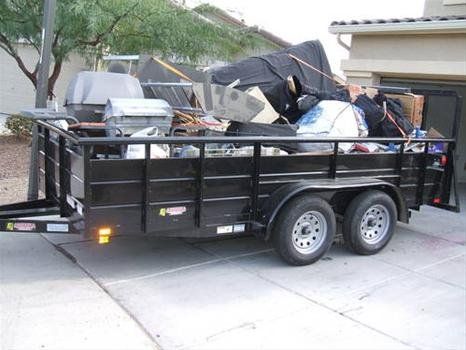 A trailer full of junk is parked in front of a house