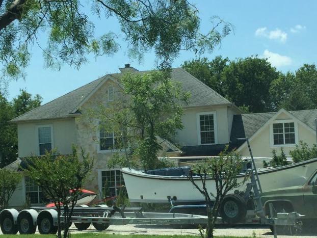 House with boat on a trailer parked in front; trees and sky in the background.