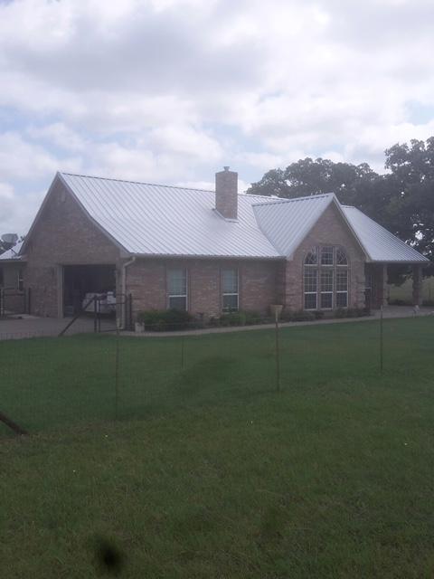 A brick house with a metal roof on a grassy lawn under a cloudy sky.