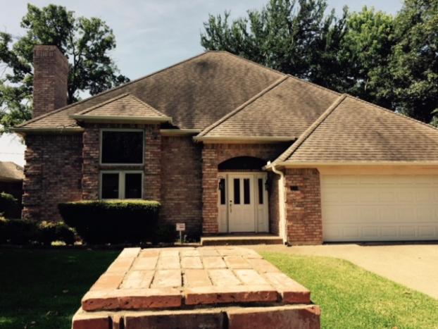 Brick house with a light-colored garage door and white front door. Overgrown roof, brick walkway, and green lawn.