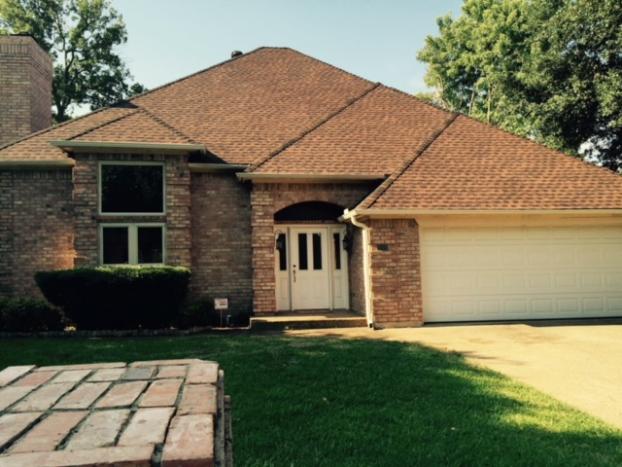 Brick house with brown roof, white garage door, and green lawn on a sunny day.
