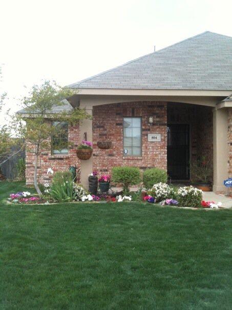 Brick house with colorful flowerbeds and lush green lawn.