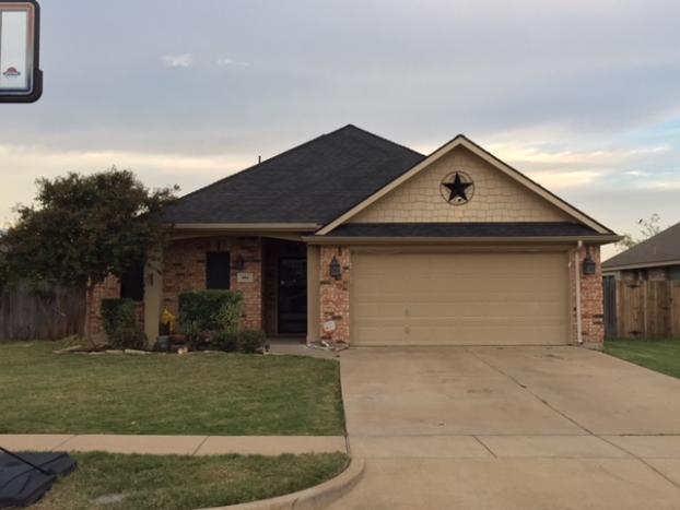 House with tan garage door, brick and tan siding, and black roof. A star decorates the gable.