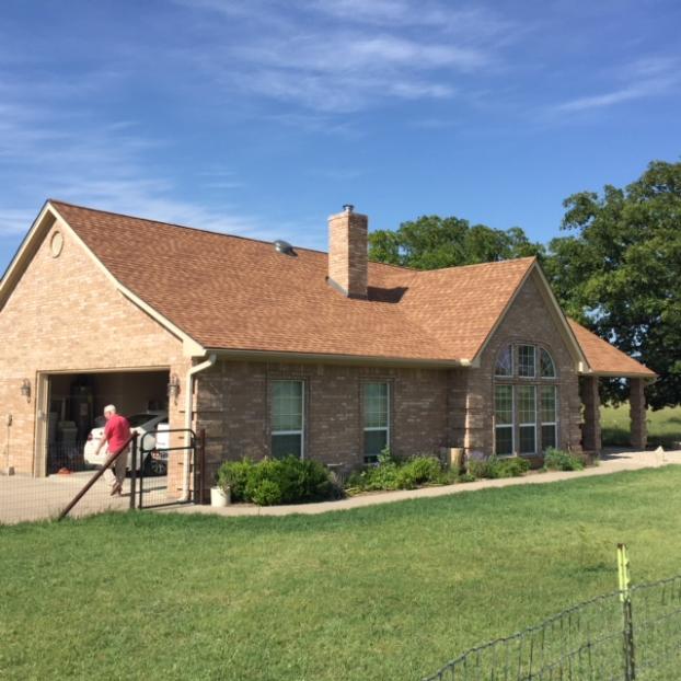 Brick house with brown roof, garage, and chimney on a sunny day. A person walks near the garage.