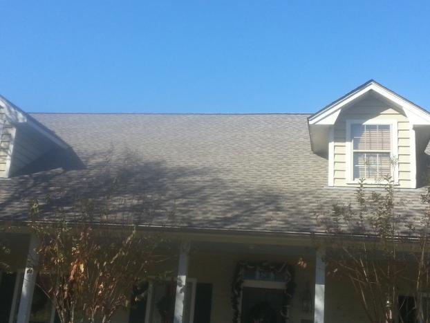 House with gray roof, beige siding, and two dormer windows against a clear blue sky.