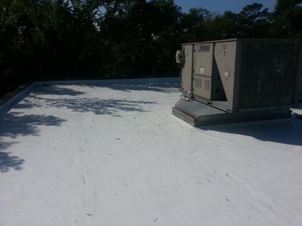 A flat, white roof with an air conditioning unit. Trees are in the background.