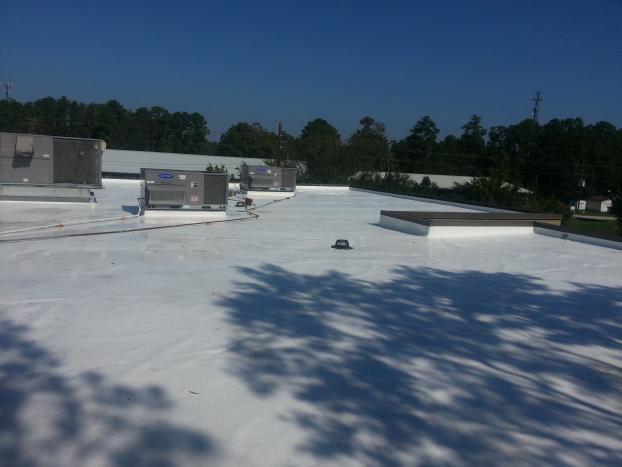 White commercial flat roof with HVAC units, skylight, and trees under a blue sky.
