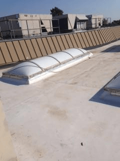Skylight on a flat roof, white and tan building in the background. Sunny day.