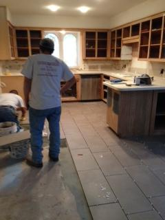 Two workers installing tile in a kitchen with new cabinets and an island.