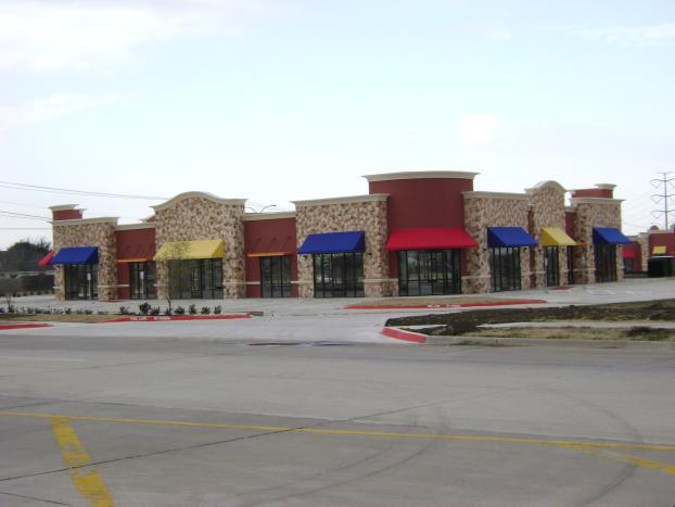 Strip mall with red, tan, and blue awnings, on a concrete lot, overcast sky.