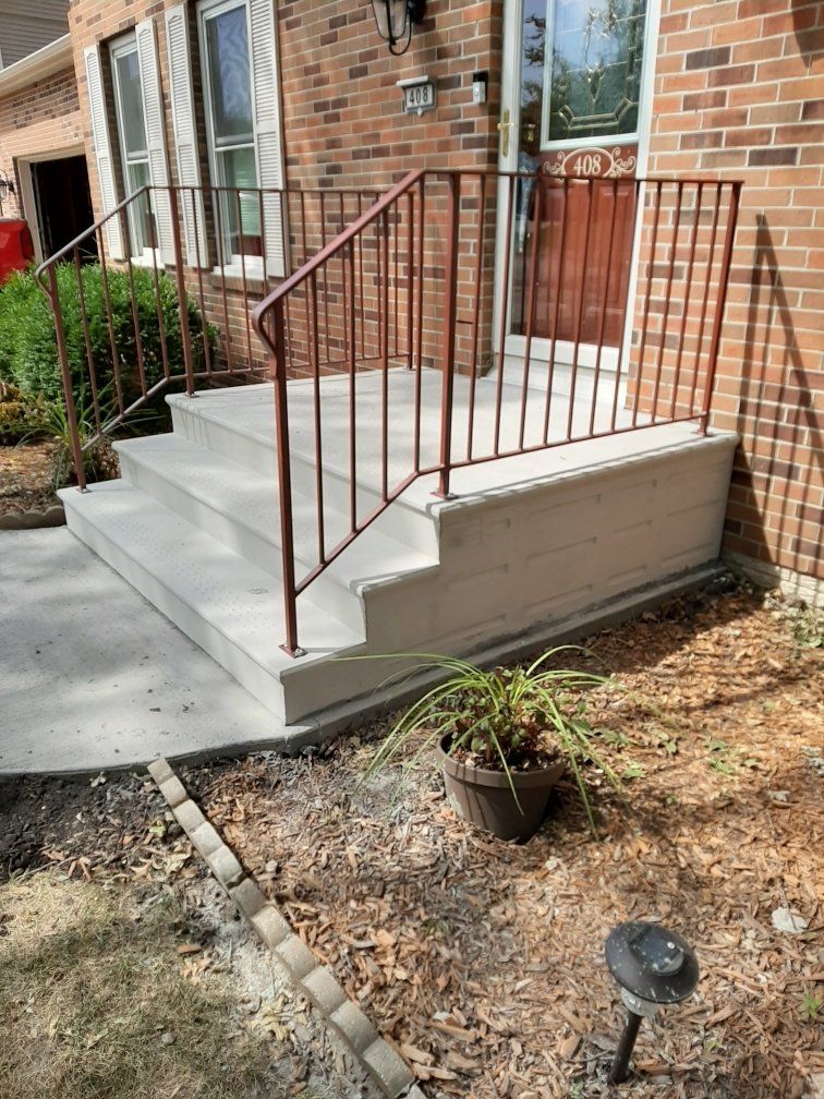 Front porch with concrete steps and rust-colored metal railing beside a brick house.
