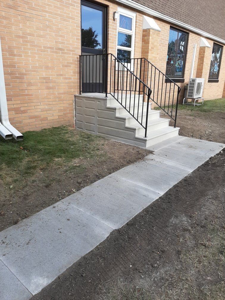 Apartment entrance with concrete steps, black handrail, and a sidewalk leading to the door