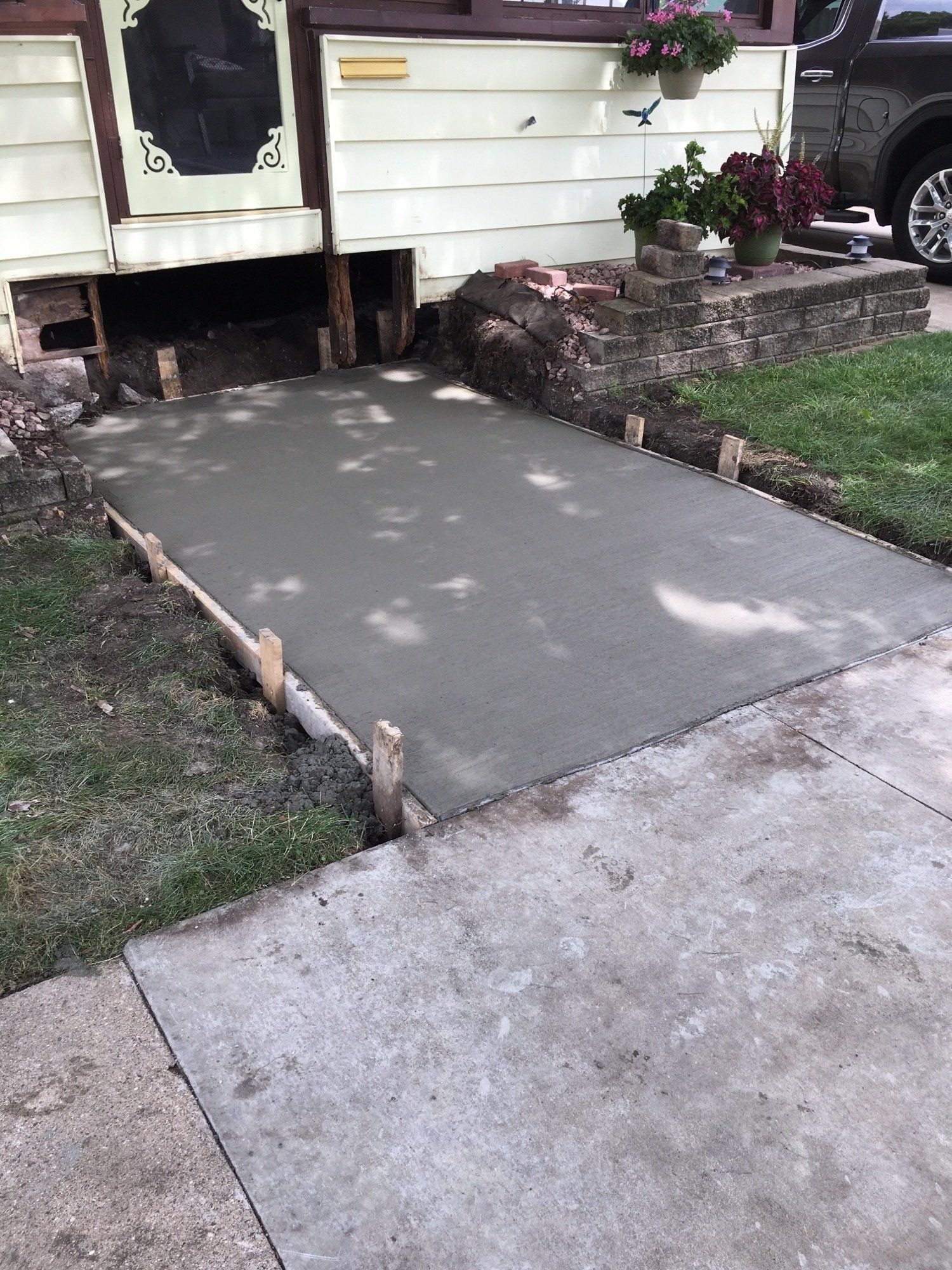Freshly poured concrete wheelchair ramp leading to a house entrance with short wooden forms and stone border