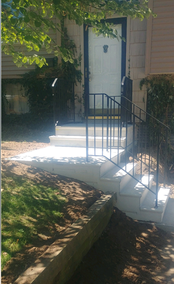 Front steps leading to a white front door with a black railing and shaded walkway