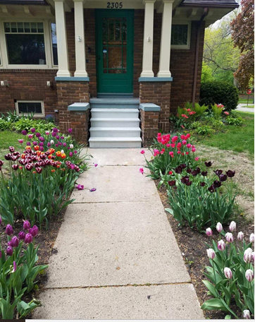 Front porch with teal door, brick house, and a walkway lined with colorful flowers