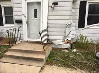 Front entry of a house with cracked steps, a damaged railing, and broken siding near the porch