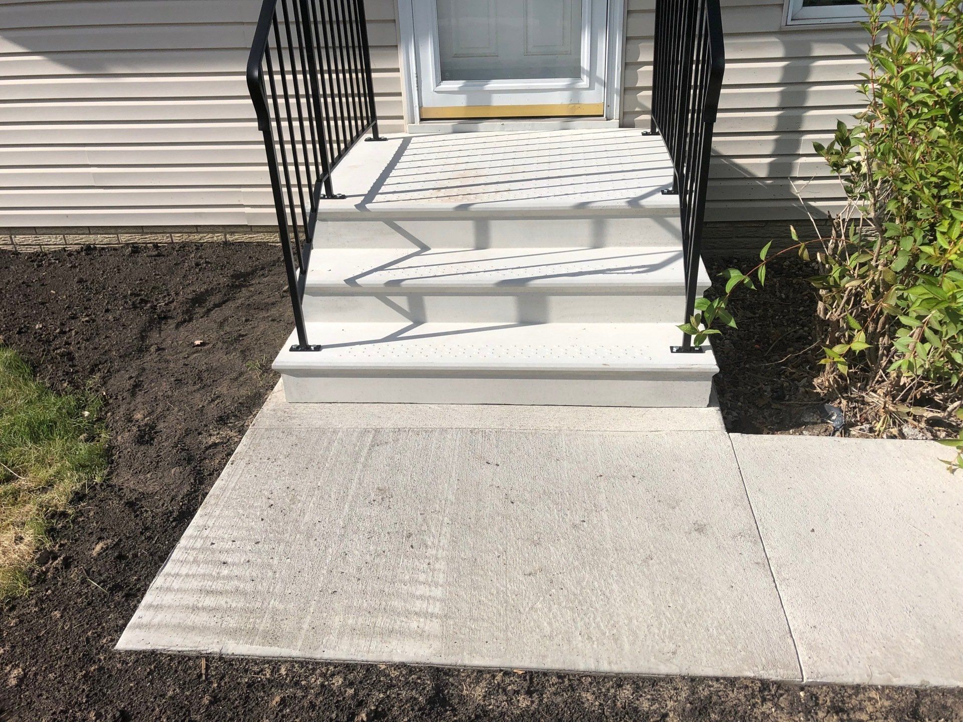 Front steps with black railings leading to a white front door and concrete walkway