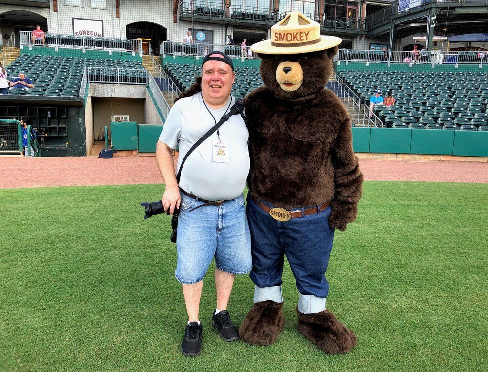 A man is standing next to a bear mascot on a baseball field.