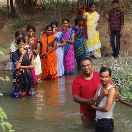 A group of people standing in a river with one man in a red shirt