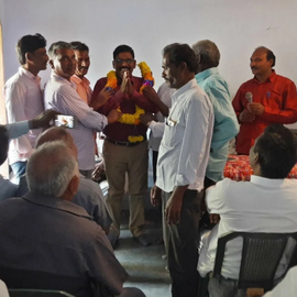 A group of men are gathered in a room and one of them is wearing a red shirt