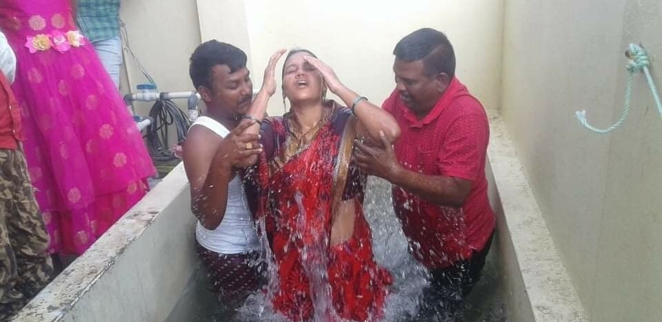 A woman in a red dress is being baptized by two men in a bathtub.