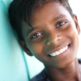 A young boy is smiling and leaning against a wall