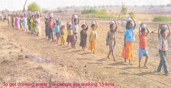 A group of children are walking in a line carrying water buckets on their heads.