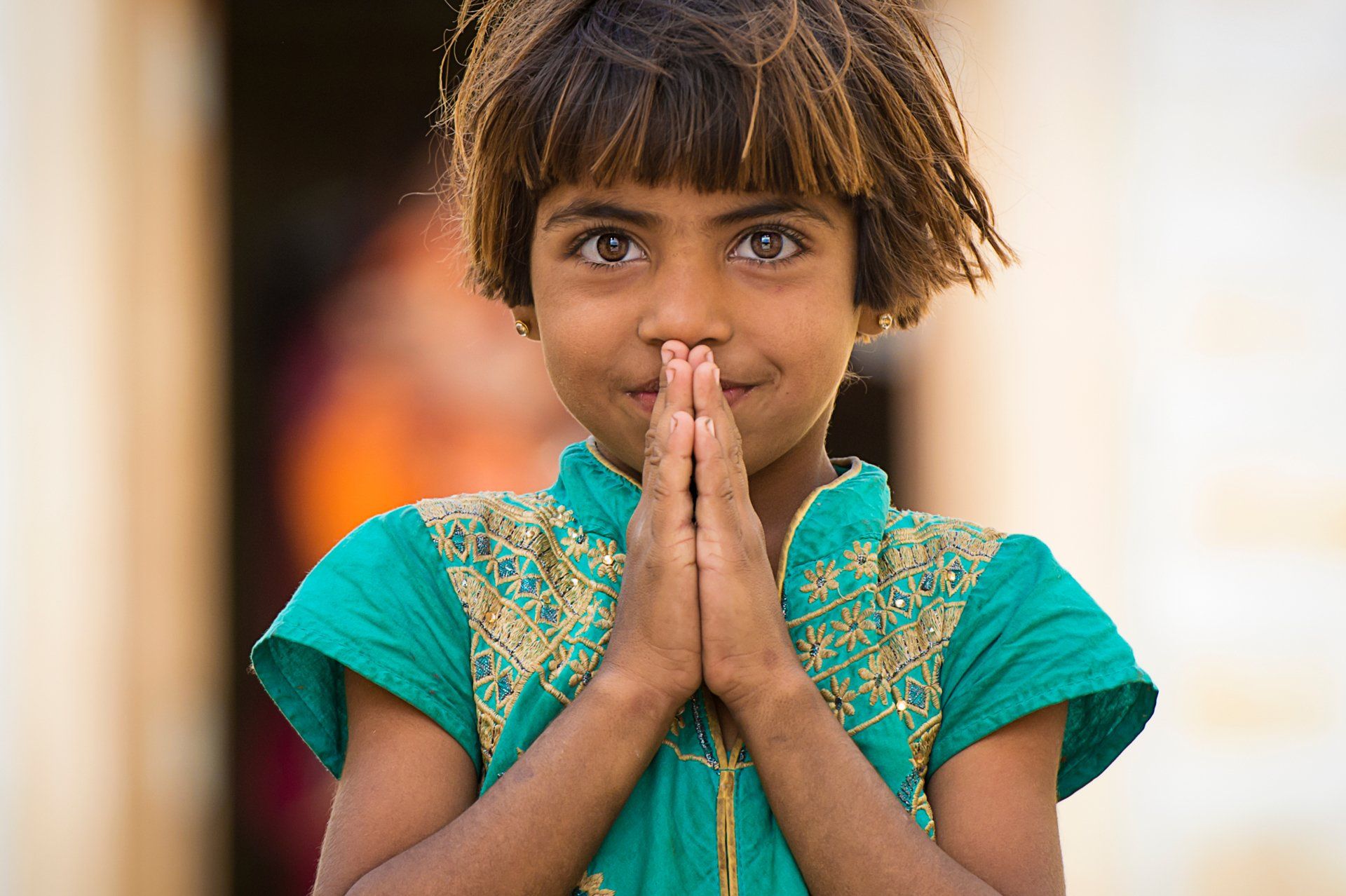 A young girl in a green shirt is holding her hands together and smiling.