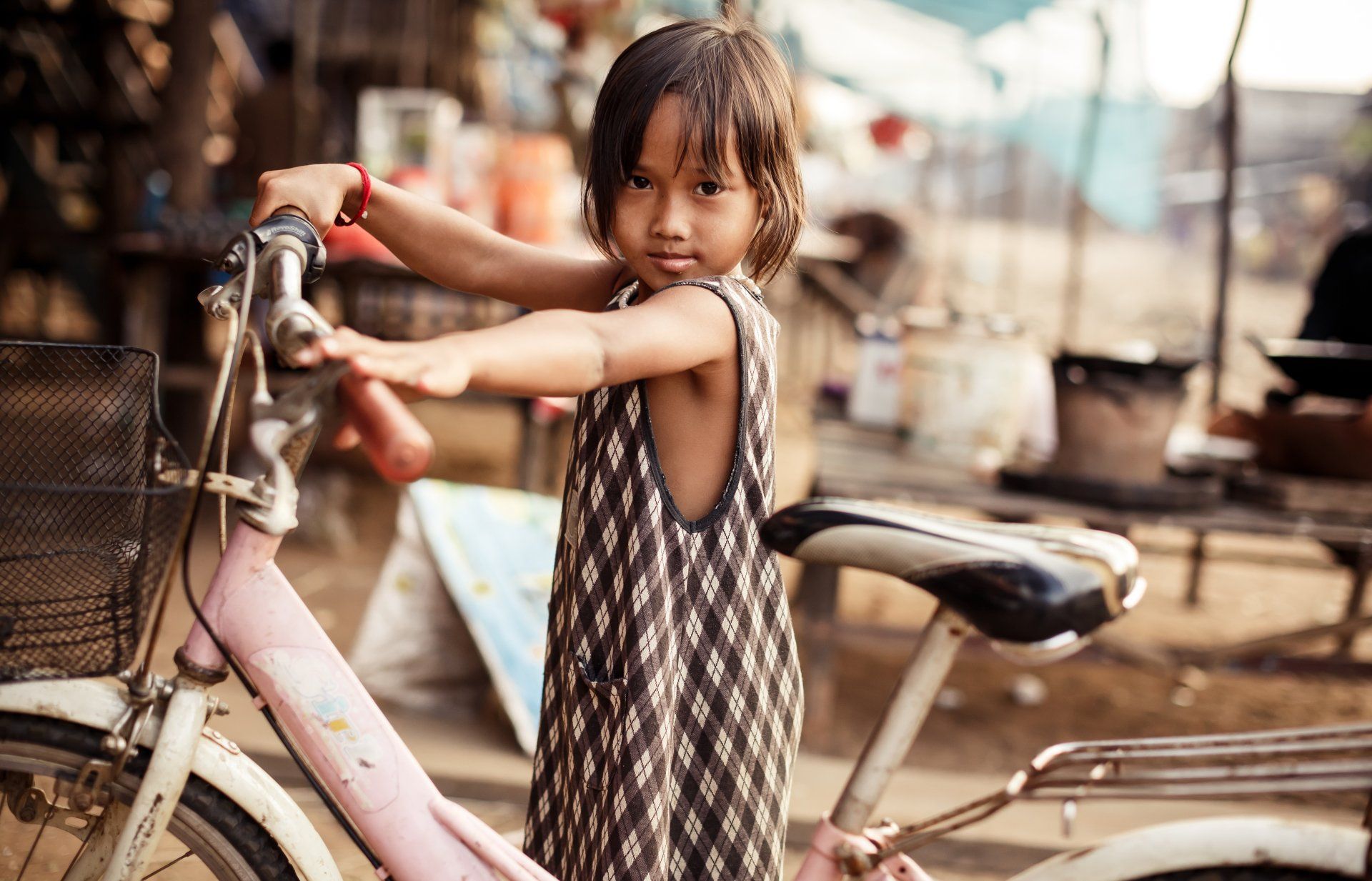 A little girl is standing next to a pink bicycle.