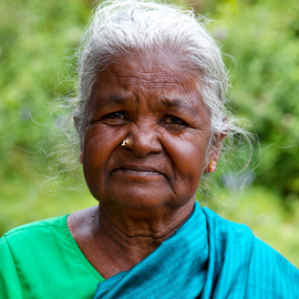 An older woman wearing a green shirt and a blue scarf looks at the camera