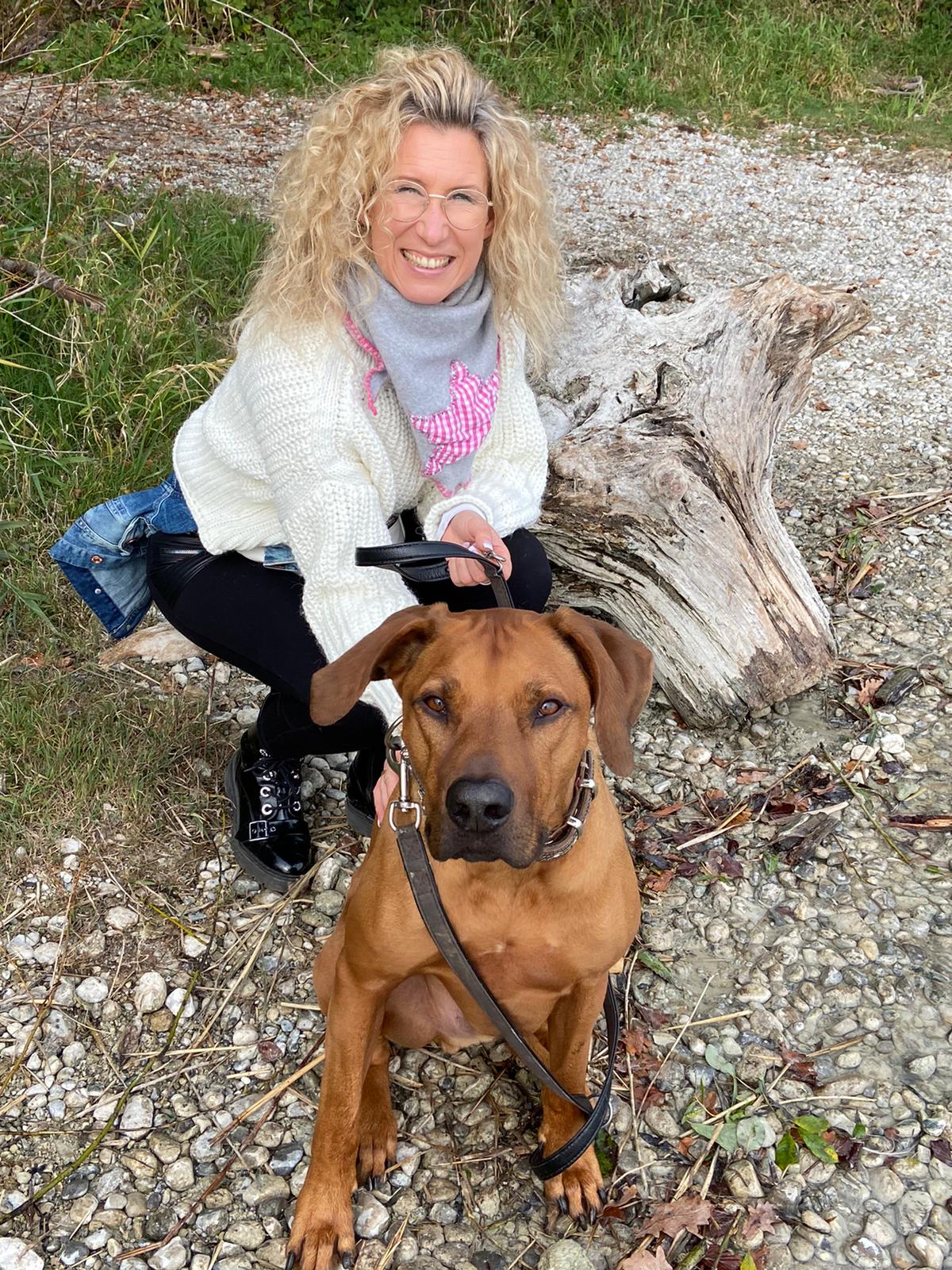 Eine Frau kniet neben einem braunen Hund an der Leine.