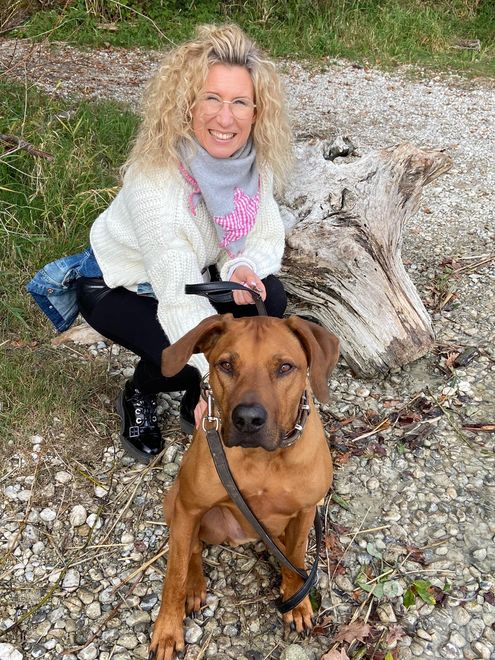 Eine Frau kniet neben einem braunen Hund an der Leine.