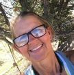 A woman wearing glasses is smiling in front of a tree.
