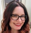 A woman wearing glasses and red lipstick is smiling for the camera.