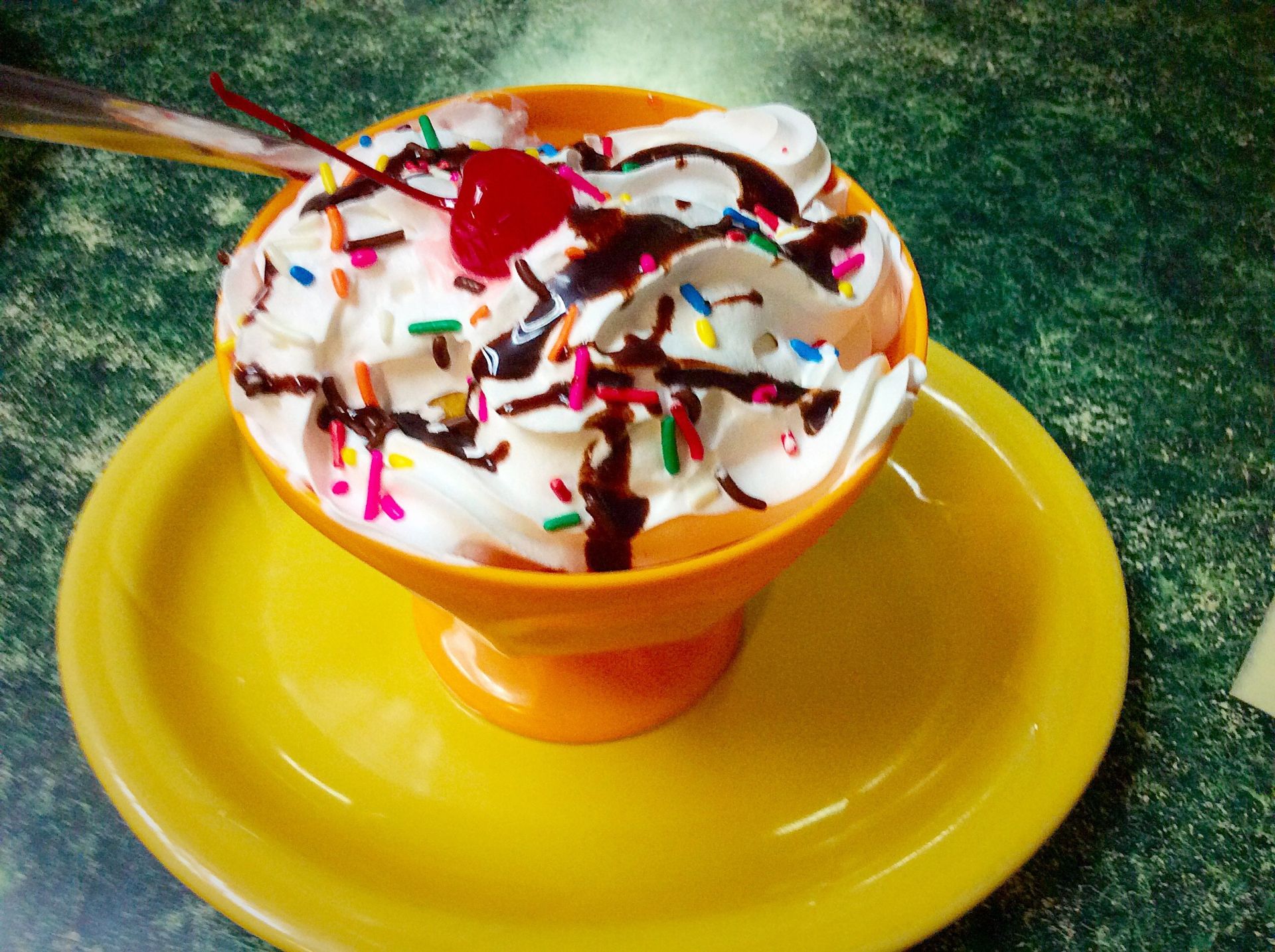 Sundae in a yellow dish: whipped cream, chocolate syrup, sprinkles, cherry.