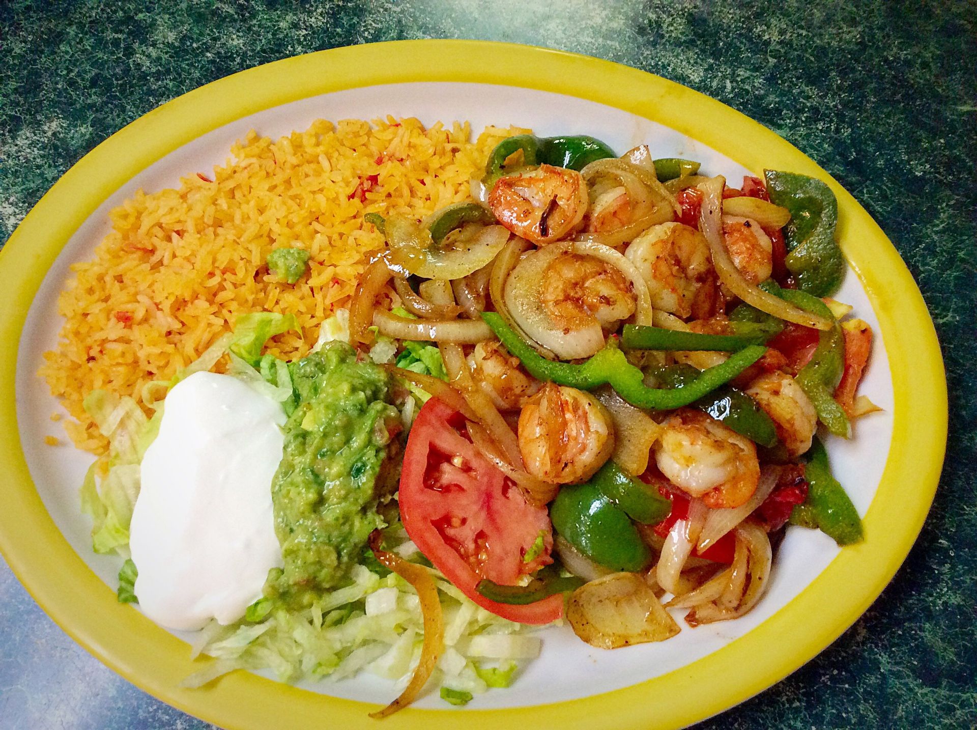 Shrimp fajita platter with rice, guacamole, sour cream, and tomato slices.